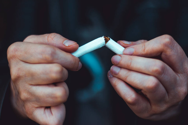 Κλείσιμο ενός νεαρού ατόμου τα χέρια σπάζοντας ένα λευκό τσιγάρο στη μέση Τοξική και επικίνδυνη συνήθεια Έννοια εικόνα για την ημέρα κατά του καπνίσματος και διακοπή εθισμού - Φωτογραφία, εικόνα