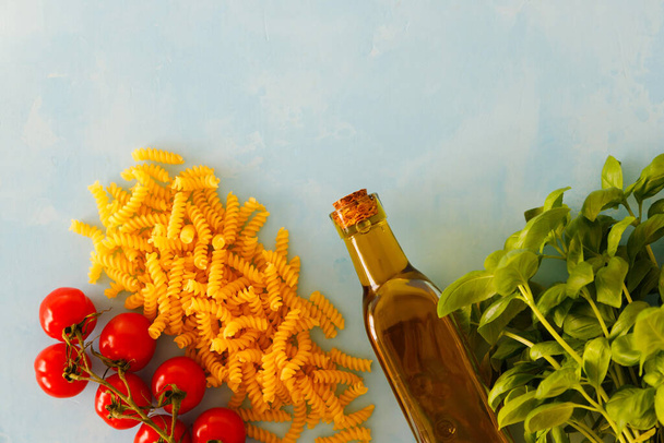 The concept of cooking pasta with pesto. Spaghetti, tomatoes, basil, a bottle with olive oil on a blue background. Place for text. - Photo, Image