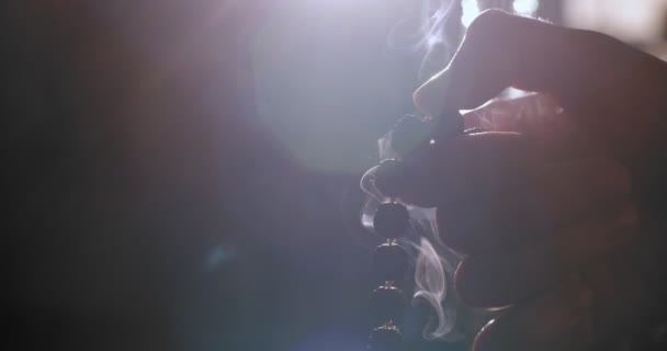 Makro detailní pohled na prsty počítání korálků na tmavém pozadí s podsvíceným kouřem kadidla. Zblízka ruce drží dřevěný růženec uvnitř přirozené světlo. Myšlenka meditace náboženské spirituality - Záběry, video