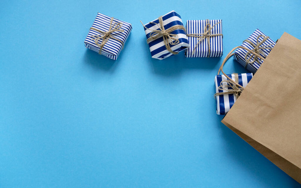 Gift boxes fall out of a paper bag on a blue background. Set of surprises in decorated packages. - Zdjęcie, obraz