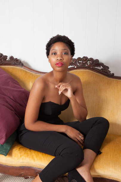 Mujer negra pensativa sentada en un sofá de oro
 - Foto, imagen