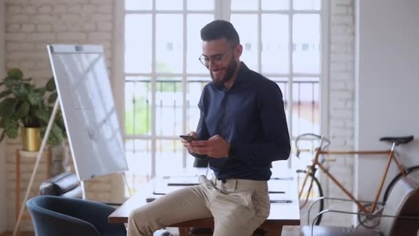 Smiling young entrepreneur using smartphone mobile apps in modern office - Metraje, vídeo