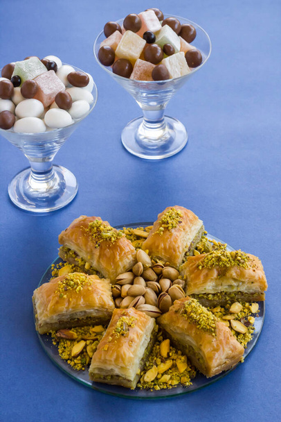 Traditioneel Turks gebak Dessert, Baklava ontworpen op glasplaat met pistachenoten. Op blauwe achtergrond met snoepbakjes - Foto, afbeelding