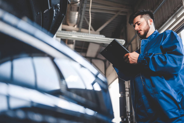 Mécanicien de voiture écrit plan de réparation sur presse-papiers. Travailleur de service automobile masculin - Photo, image