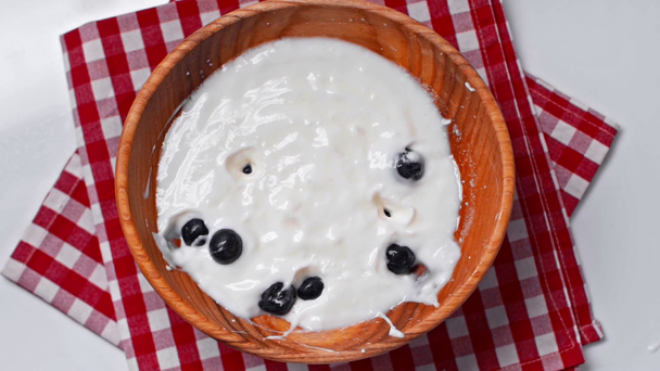 bovenaanzicht van bosbessen die in een kom vallen met verse yoghurt geïsoleerd op wit - Video