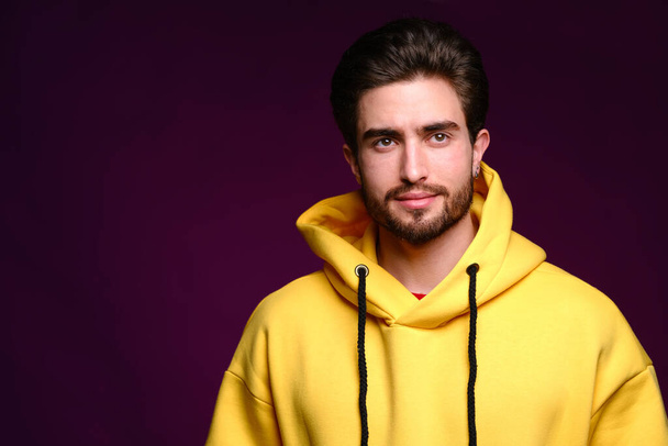 A young man of 25-30 years in yellow sweatshirt emotionally poses on a purple background.  - Fotó, kép