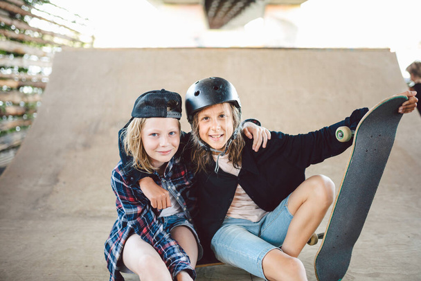 Eine Gruppe Skateboarder-Kinder posiert auf einer Rampe im städtischen Skatepark. Freunde verbringen aktive Zeit mit Skateboardfahren im Park. Spielplatz für Straßensport. Jugend, Miteinander und Freundschaftskonzept. - Foto, Bild