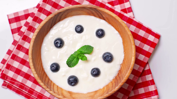 vista dall'alto di gustosi mirtilli in ciotola con yogurt fresco isolato su bianco - Filmati, video