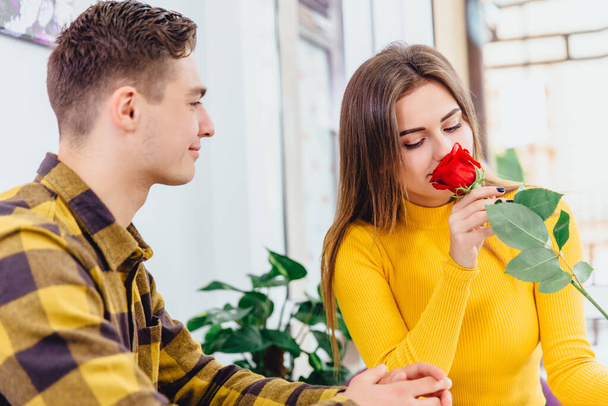 Young couple in love sitting in cafe celebrating their honymoon, man brought a red rose for his beautiful young woman,. - Foto, immagini