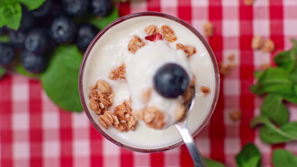 top view of man holding spoon near yogurt with granola in glass - Footage, Video