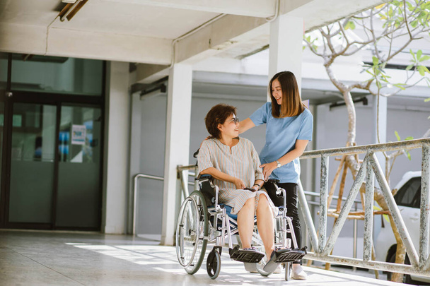 Χαμογελώντας φυσιοθεραπευτής φροντίζει τον ευτυχισμένο ηλικιωμένο ασθενή σε αναπηρική καρέκλα - Φωτογραφία, εικόνα