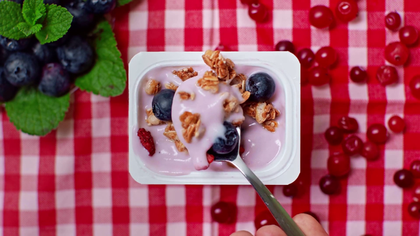 top view of man holding spoon near yogurt with granola and berries in glass - Footage, Video
