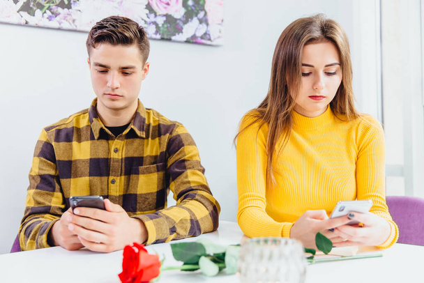 Couple has a date in cafe, but instead of communicating they are using smartphones, reading news, chatting online, ignoring presence of one another. - Foto, Bild