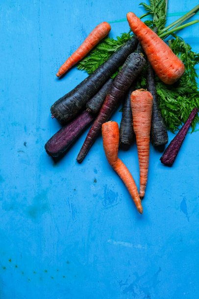 Orange and purple carrots, green stems on grunge blue background, top view. Vertical image with copy space - Photo, Image