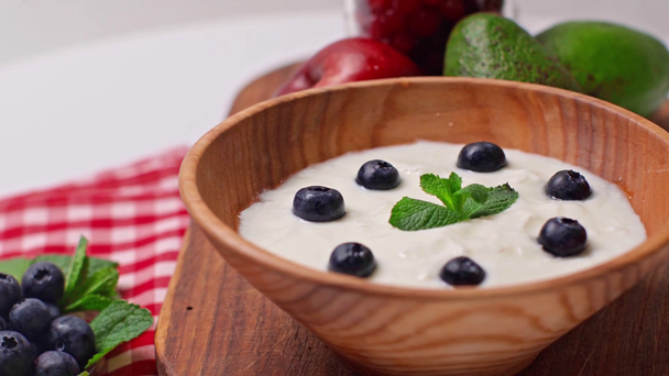 selective focus of bowl with yogurt and blueberries near fruits on white - Footage, Video