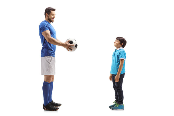 Full length profile shot of a man in a suit giving football to a boy isolated on white background - Fotoğraf, Görsel