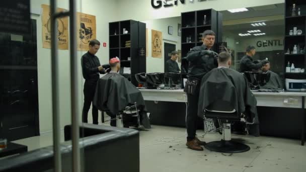 Kaksi kokenutta mestaria mustissa käsineissä tekevät hiustenleikkuun asiakkaalle parturissa - Materiaali, video