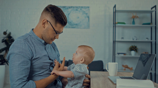 гарний батько тримає в руках милий немовля син біля ноутбука
  - Кадри, відео