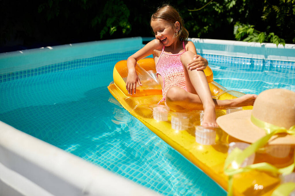 Kleines Mädchen mit Hut entspannt im Schwimmbad, schwimmt auf aufblasbarer gelber Matratze und hat Spaß im Wasser im Familienurlaub, tropischer Ferienort. - Foto, Bild