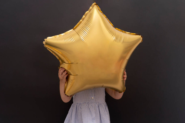 Closeup of caucasian child hanging gold star balloon with hands and hidding face - Photo, Image