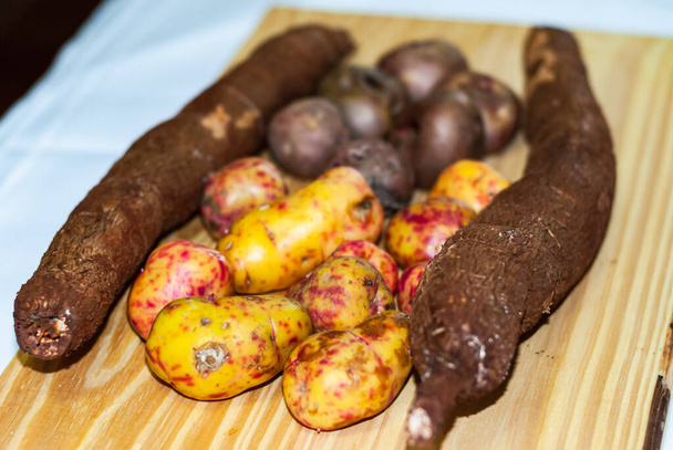 Surowa yucca na drewnianym stole, Manihot esculenta. (Cassava surowy bulw) z ziemniakami regionalnymi z Andów na rynku w Peru, Boliwii, Argentynie, Ameryce Południowej. - Zdjęcie, obraz