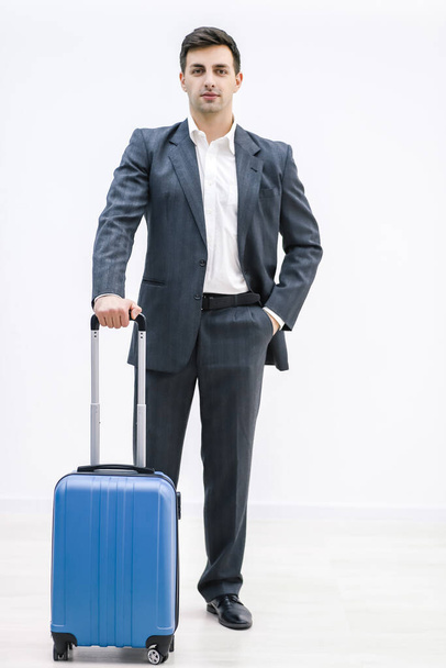 A young handsome businessman in a suit, stands with a suitcase, at the station, at the airport. - Foto, Bild