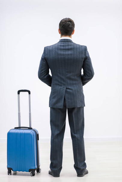 Rear view of successful businessman in suit standing in airport terminal, with suitcase over white background. - Zdjęcie, obraz