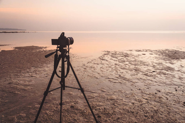 Réglage de l'appareil photo au trépied pour prendre une photo ou une vidéo du lever ou du coucher du soleil. mise au point sélective à la caméra mer floue en arrière-plan. vue sur la mer dans écran moniteur. effet de lumière d'image filtrée ajouté - Photo, image