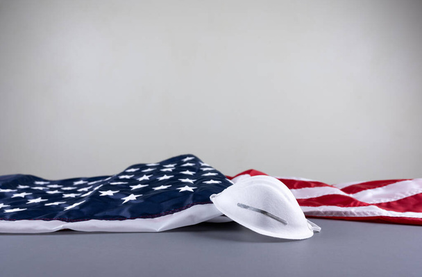 Gezichtsmasker en Amerikaanse vlag op grijze achtergrond tijdens pandemie.4 juli, Veteranendag, Vlaggendag, 14 juni, Dag van de Arbeid, herdenkingsdag, Vakantie concept. - Foto, afbeelding