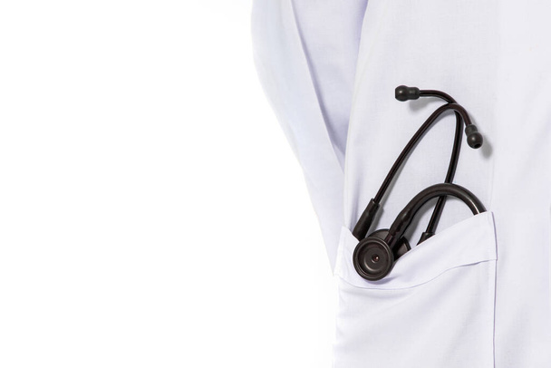 Ένας όρθιος γιατρός με μακρύ λευκό νοσοκομειακό φόρεμα με μαύρο στηθοσκόπιο στην τσέπη. Απομονωμένα σε λευκό φόντο. - Φωτογραφία, εικόνα