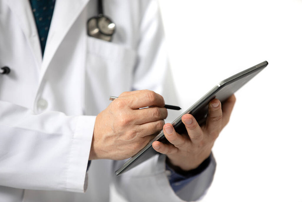 Un médico de pie con una larga bata blanca de hospital escrito en una tableta. Aislado sobre fondo blanco
. - Foto, Imagen