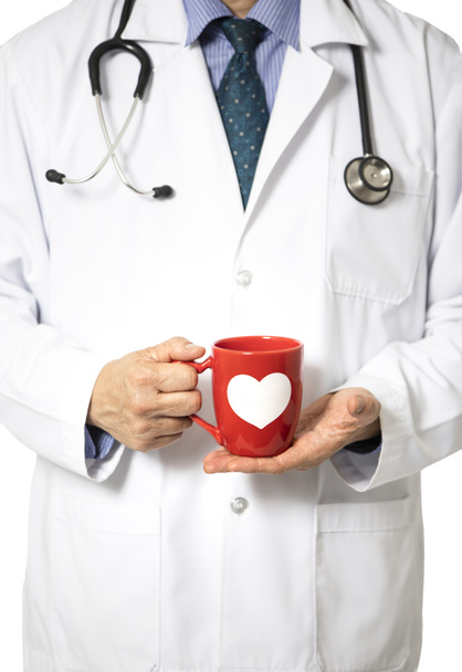 Beyaz hastane önlüklü bir erkek doktor elinde beyaz kalp desenli turuncu bir kahve kupası tutuyor. Rahat ve davetkar tıbbi personel konsepti. Beyaz arkaplanda izole. - Fotoğraf, Görsel