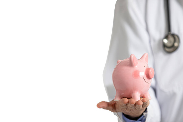 A male doctor in white hospital gown holding a pink piggy bank in his hand. Hospital expense concept. - Fotó, kép