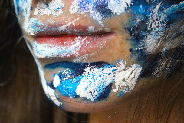 Painted face with acrylic blue and white colors. Young beautiful woman portrait, close-up photo. - Photo, Image