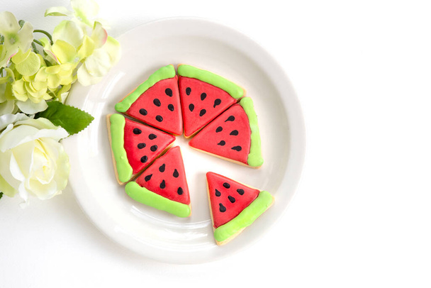 Watermelon shaped Christmas cookies on a white ceramic plate with white background.  Non traditional looking baked biscutes for the holidays.  A happy new year card concept. Template, Flat Lay. - Photo, Image