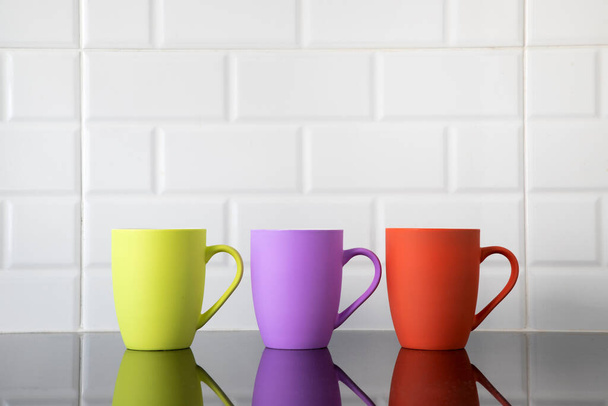Colorful coffee mugs on black granite kitchen table with their reflections on top of the counter's clean surface. - Photo, Image