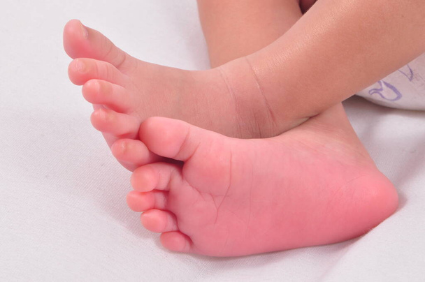 Mały różowawy miękkie stopy dziecko skrzyżowane na drugim podczas snu w białym tle. - Zdjęcie, obraz