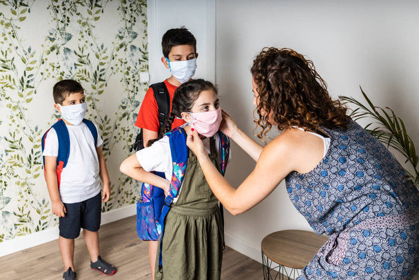 Мати кладе маски для обличчя своїм дітям, перш ніж вони підуть до школи
 - Фото, зображення