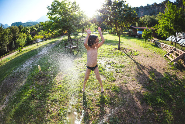 Güneşli bir günde sırılsıklam olan çocuk evin bahçesine çocuk hortumu sıkar, tatilde eğlence, bir çocuğun duyguları, çocuk eğlencesi.. - Fotoğraf, Görsel