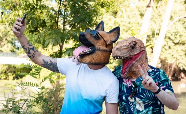 Couple à la mode portant t-rex et masque de chien, prenant un selfie - Photo, image