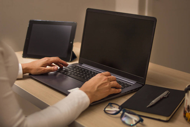 Руки женщины, работающей на ноутбуке в белой рубашке, справа очки и планшет на черном блокноте
 - Фото, изображение