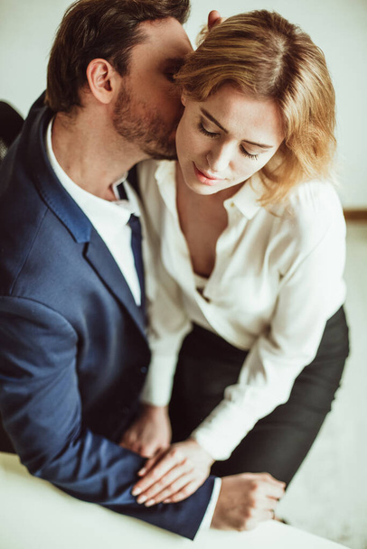 Love affair at work. Business man kisses neck of a woman sitting on his lap. Two people flirting together in office. High angle view - Foto, afbeelding