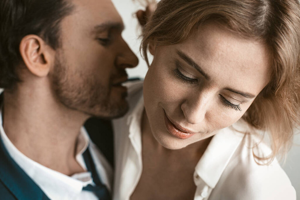 Sexy couple of business people in love. Close up portrait. Man going to kiss female neck. Selective focus on happy smiling female face in foreground - Photo, image