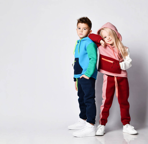 Dark haired boy and blonde girl in stylish jym suits standing back to back. Portrait isolated on light grey, copy space - Foto, Bild