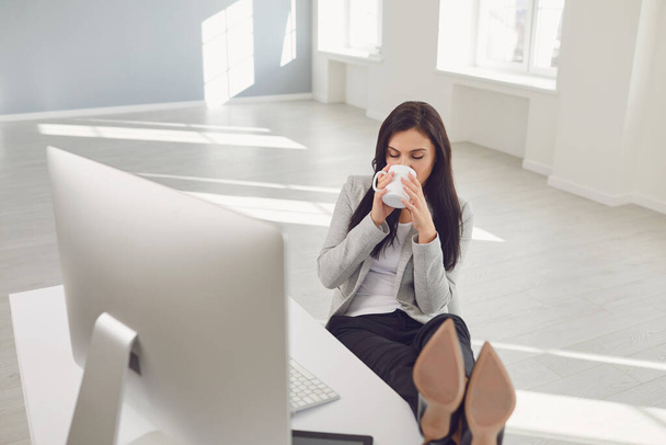 Relaxing businesswoman enjoying coffee at workplace in office - Фото, зображення
