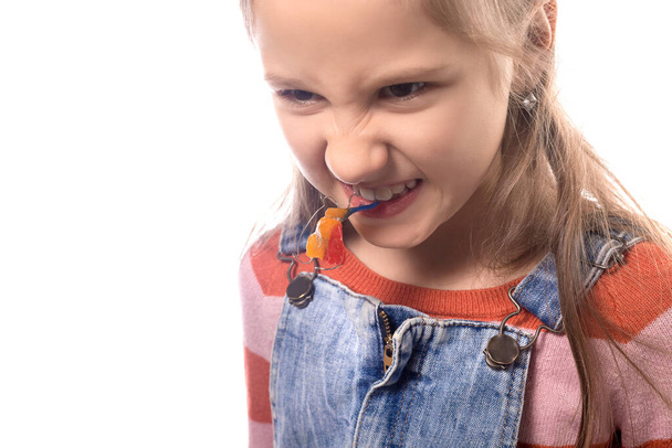 Kleines Mädchen beißt kieferorthopädisches Gerät isoliert auf weißem Hintergrund. - Foto, Bild