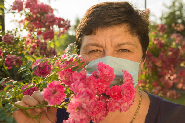 Egy középkorú nő képe. A koronavírus elleni védelem is gyönyörű lehet. Egy nő rózsákkal díszítette fel az orvosi maszkot.. - Fotó, kép
