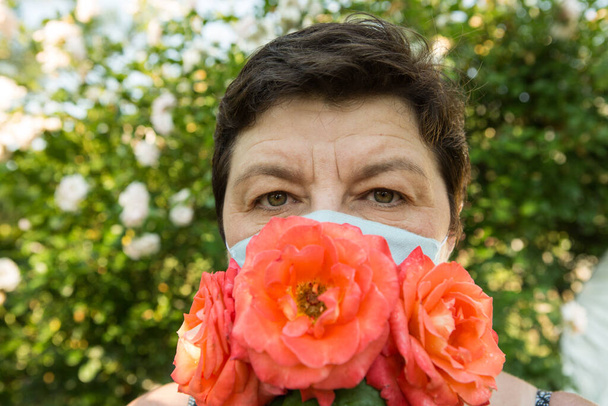 Egy középkorú nő képe. A koronavírus elleni védelem is gyönyörű lehet. Egy nő rózsákkal díszítette fel az orvosi maszkot.. - Fotó, kép