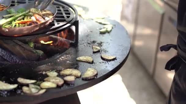 Der Koch brät die Zucchini. Gemüse vom Grill. Runder schüsselförmiger Grill mit Feuer im Inneren.  - Filmmaterial, Video