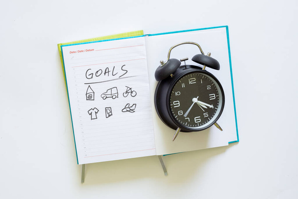 Blue open agenda and a retro black clock sitting on a white background. The word goals and hand drawings of different icons on a white paper from a binder - Photo, Image